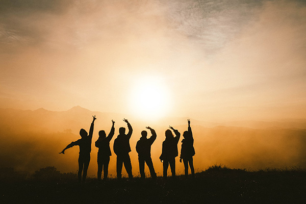 Group of six people with their arms raised, silhouetted against the sunset